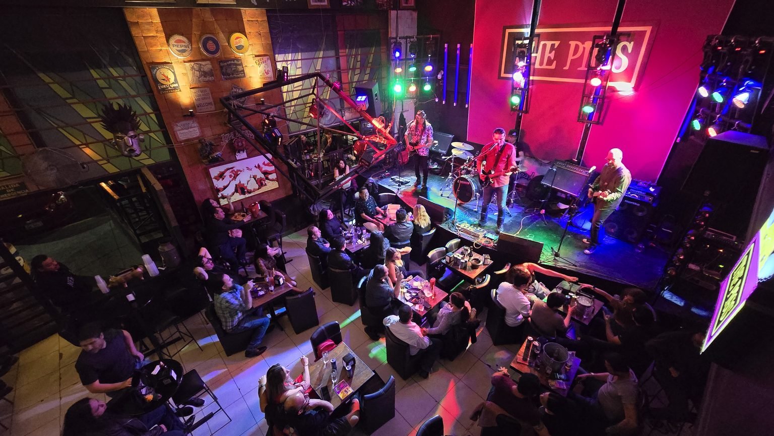 Vista desde arriba de The Pigs con música en vivo: banda en el escenario con luces de colores y mesas con clientes